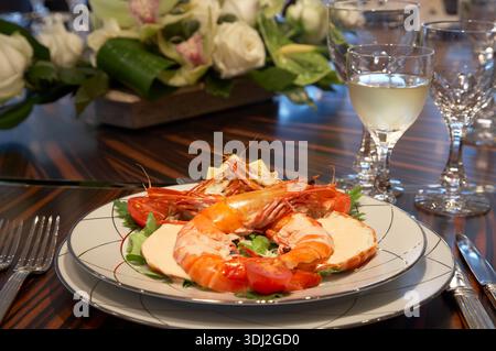Elegante piatto di pesce con gamberi giganti e verdi al tavolo formale durante la cena Foto Stock