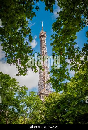 Torre Eiffel incorniciata da alberi frondosi in un parco di Parigi, che si innalza contro un cielo azzurro luminoso in un tranquillo paesaggio urbano estivo. Foto Stock