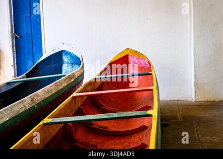 Due vivaci canoe intemprate con scafi dipinti e sedili in legno sono collocati all'interno vicino a una porta blu brillante e a una parete testurizzata Foto Stock