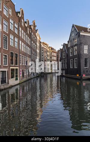 Case storiche alte e strette sui canali ad Amsterdam, Paesi Bassi. L'iconica architettura olandese si riflette nelle acque calme sotto un cielo azzurro. Foto Stock