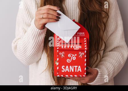 Donna che tiene una cassetta postale rossa per le lettere a Babbo Natale. Tradizione natalizia e decorazioni natalizie. Concetto di stagione natalizia. Accogliente stile di vita invernale all'interno. Foto Stock