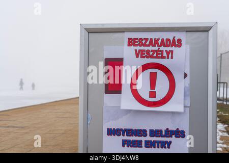 Cartello segnaletico „PERICOLO: RISCHIO DI ROTTURA LUNGO la passeggiata di Siófok, accanto al lago Balaton ghiacciato. Foto Stock