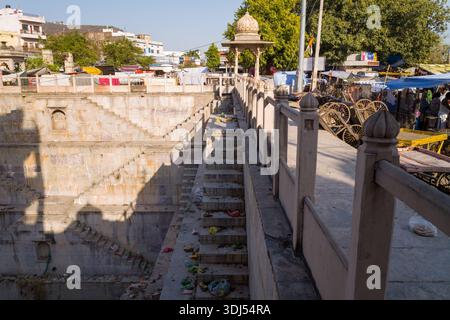 Bundi, India - 19 marzo 2022: Un grande gradino in pietra con scalinate simmetriche e un padiglione a cupola è visto con detriti sui gradini, bancarelle del mercato, lavanderia, carrelli e persone lungo il passaggio superiore durante il giorno. Foto Stock