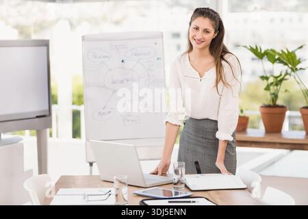 Computer portatile e notebook aperti sono seduti su un tavolo da conferenza in legno vicino a lavagna a fogli mobili e piante. Presentatore, professionista, luce del giorno, ufficio, collaborazione, Foto Stock