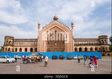 Lucknow, India - 16 marzo 2024: L'immagine mostra lo storico cancello Rumi Darwaza con impalcature e barriere blu di costruzione, auto parcheggiate, venditori ambulanti con carrelli e gruppi di persone in primo piano sotto la luce del giorno. Foto Stock