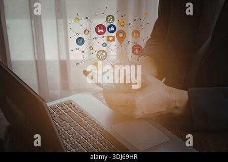 Immagine che mostra le mani di una persona che interagiscono con varie icone digitali che fluttuano sopra un notebook. Le icone rappresentano diversi social media e netwo Foto Stock