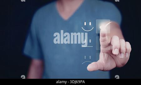 Una persona che indossa una camicia blu interagisce con un'interfaccia digitale che mostra un volto sorridente, rappresentando probabilmente un'esperienza utente o un feedback positivo Foto Stock
