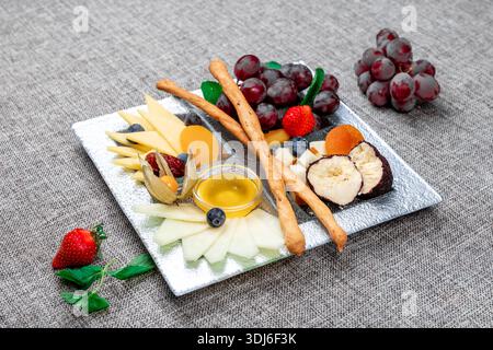 Un vassoio di formaggi gourmet splendidamente organizzato con vari tipi di formaggio a fette, uva rossa, fragole fresche, mirtilli, fisti, e dri Foto Stock