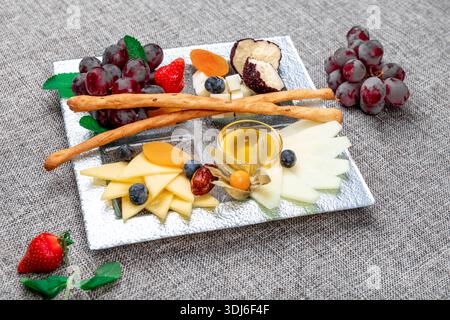 Un vassoio di formaggi gourmet splendidamente organizzato con vari tipi di formaggio a fette, uva rossa, fragole fresche, mirtilli, fisti, e dri Foto Stock