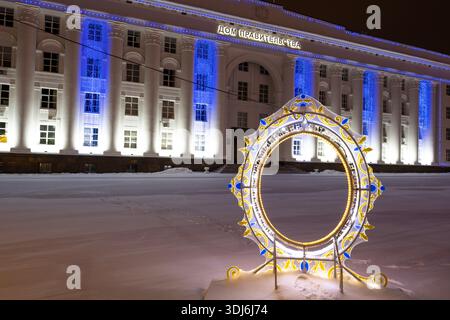 Ulyanovsk, Russia - 14 febbraio 2022: Arco di Capodanno illuminato in primo piano e sede del governo sulla piazza centrale coperta di neve della città Foto Stock