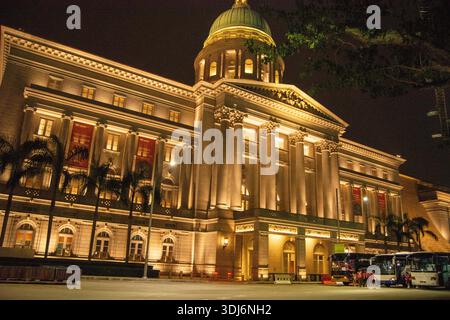 Un edificio storico splendidamente illuminato di notte, che mostra dettagli architettonici e una cupola, circondato da palme Foto Stock