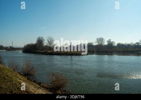 Una tranquilla scena fluviale con un faro su una piccola isola, circondata da alberi e cielo azzurro Foto Stock