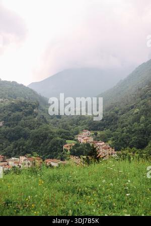 Piccolo villaggio tradizionale accoccolato in una lussureggiante valle di montagna Foto Stock