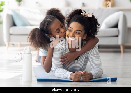 Buona madre nera e figlia coccolarsi mentre praticano lo yoga Foto Stock