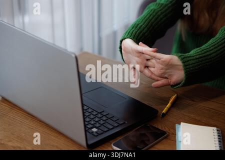 Primo piano di una donna che allunga mani e dita durante la pausa di lavoro alla scrivania per alleviare la tensione dall'uso del computer. Foto Stock