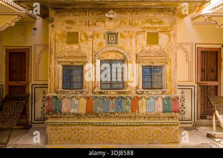Jaipur, India - 15 marzo 2022: L'immagine mostra una facciata decorativa con tre finestre con persiane blu, disegni dipinti ornati e colorate opere di rilievo nel cortile interno di una vecchia casa tradizionale, con porte in legno e pareti a motivi visibili su entrambi i lati. Foto Stock
