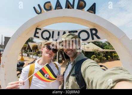 Segno di confine nord-sud - Equatore in Uganda, una giovane coppia scatta un selfie con la bandiera ugandese. Foto Stock