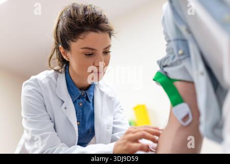 Flebotomo amichevole dell'ospedale che raccoglie il campione di sangue dal paziente in laboratorio. Preparazione per l'esame del sangue da parte di medico donna uniforme medica sulla tabella i Foto Stock