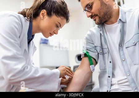 Flebotomo amichevole dell'ospedale che raccoglie il campione di sangue dal paziente in laboratorio. Preparazione per l'esame del sangue da parte di medico donna uniforme medica sulla tabella i Foto Stock