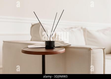Interni minimalisti con diffusore di canne nere su un tavolo rotondo in legno accanto a un divano beige, creando un soggiorno tranquillo, elegante e moderno Foto Stock