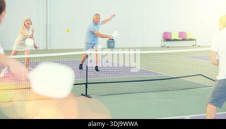 Coppia di donne anziane e uomini che giocano a doppio pickleball al coperto Foto Stock