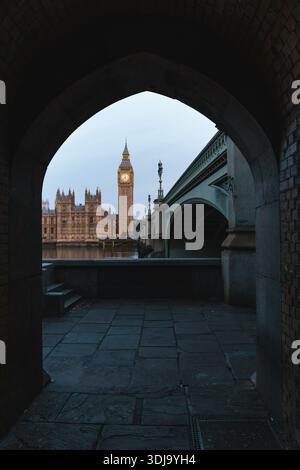 Il Big Ben e il Palazzo di Westminster sono visti attraverso un arco di pietra accanto al Westminster Bridge all'ora blu, Londra, Inghilterra, Regno Unito Foto Stock