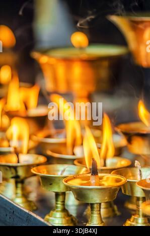 Più lampade a olio in ottone con fiamme accese si siedono vicine tra loro, emettendo una calda luce soffusa in un ambiente rituale Foto Stock