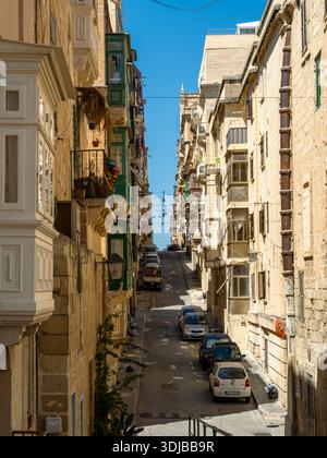 La Valletta, Malta - 8 aprile 2024: Strada stretta e ripida a la Valletta fiancheggiata da edifici storici in pietra calcarea e tradizionali balconi in legno maltese. Par Foto Stock