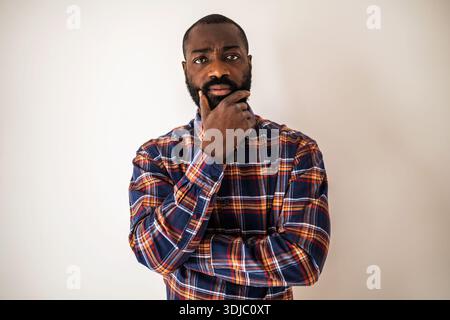 Pensivo uomo nero in una camicia accogliente che si stende sul muro, guarda la fotocamera e pensa. Foto Stock