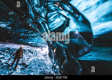 Donna con faro esplora la grotta di ghiaccio in Islanda Foto Stock