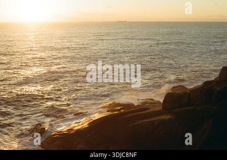 Tramonto sull'oceano con onde che si infrangono contro le rocce Foto Stock