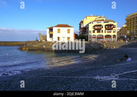 Puerto de la Cruz, 01152026 - Coastal Buildings e Rocky Beach con mare calmo e cielo limpido Foto Stock