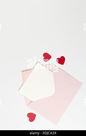 Vista dall'alto della busta rosa, cartellino bianco su sfondo bianco. San Valentino, cuori rossi, amore. Postare la stesa piatta, copiare lo spazio. Foto Stock