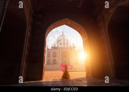 Vista posteriore di una giovane donna in un sari in piedi davanti al Taj Mahal che tiene un scialle sopra la testa al tramonto, Agra, Uttar Pradesh, India, Foto Stock