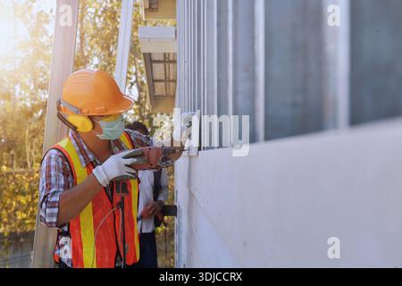 Vista laterale ravvicinata di un operaio edile che indossa indumenti da lavoro protettivi e una maschera di lavoro su un edificio, Thailandia Foto Stock