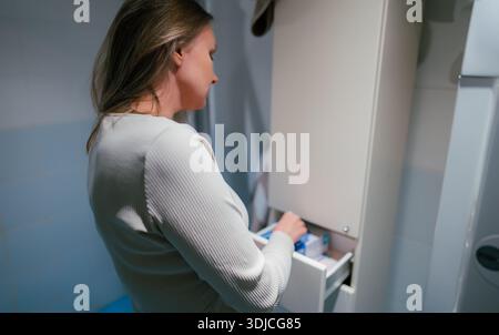 Donna che prende prodotti per l'igiene femminile dal cabinet. Foto Stock