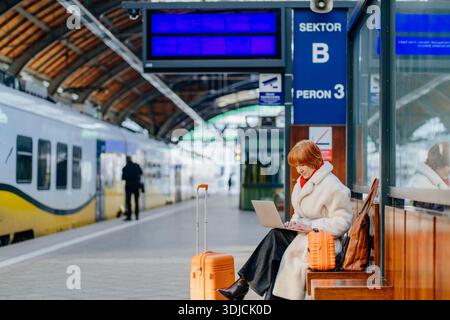 Donna rossa caucasica di mezza età sicura che sta pianificando un lavoro con un laptop durante la fermata del treno Foto Stock