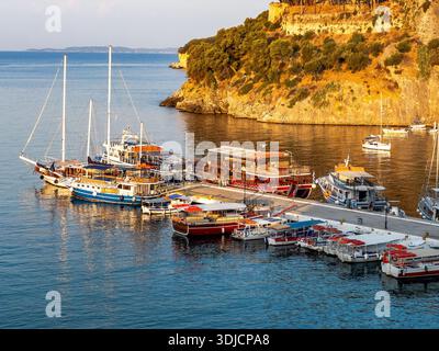 Barche ormeggiate nel porto di Parga, in Grecia, con case colorate e fortezza storica sul fianco della collina, illuminate dalla calda luce dell'alba lungo il Foto Stock