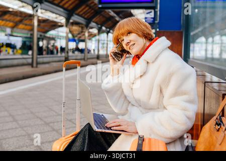 Donna rossa caucasica di mezza età che fa una chiamata di lavoro alla stazione ferroviaria Foto Stock