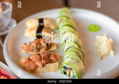 Un piatto di sushi con vari panini e guarnizioni. Il sushi include pesce fresco, avocado e riso, servito con wasabi e zenzero. Foto Stock