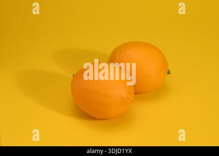 Due limoni su sfondo giallo. Le arance sono rotonde e hanno un colore arancione brillante. Lo sfondo è giallo, il che crea un caldo e invitante Foto Stock