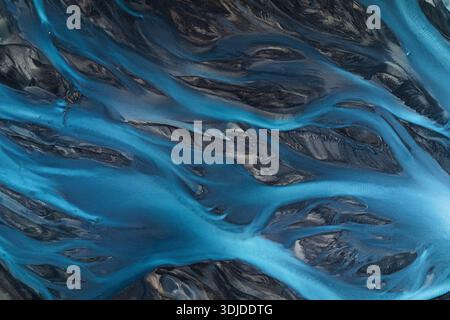 Vista aerea dei fiumi glaciali che si intagliano attraverso l'oscuro paesaggio vulcanico, creando un affascinante contrasto di blu ghiaccio contro il terreno aspro, Sel Foto Stock