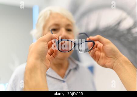 Mani tagliate di un medico maschio che dà gli occhiali a una donna anziana durante il controllo oculare in clinica oftalmologica Foto Stock