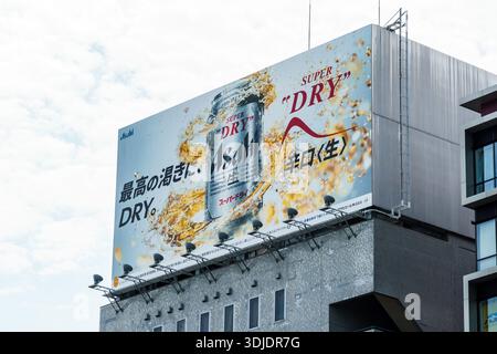 Tokyo, Giappone - 6 agosto 2024: Un grande cartellone per la birra Asahi Super Dry domina lo skyline di Tokyo, Giappone, mostrando le immagini iconiche del marchio Foto Stock