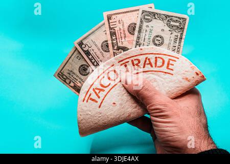 Mano che tiene la tortilla con IL COMMERCIO DI TACO e la valuta Foto Stock