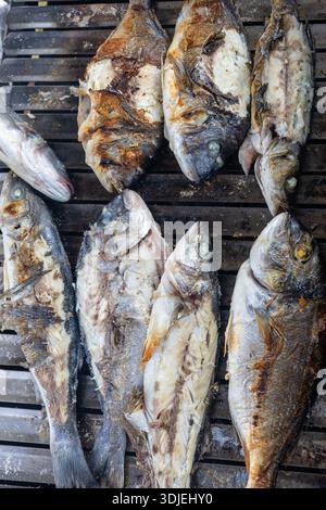 Una fila di pesce intero grigliato su un barbecue, con pelle croccante e segni di ciccioli. Scena di cucina all'aperto con un fascino rustico e saporito, adatto a se stesso Foto Stock
