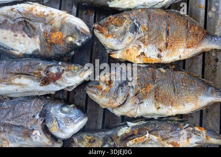 Una fila di pesce intero grigliato su un barbecue, con pelle croccante e segni di ciccioli. Scena di cucina all'aperto con un fascino rustico e saporito, adatto a se stesso Foto Stock