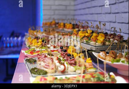 Spuntini e stuzzichini gourmet sono ben disposti su piatti, impreziositi dall'illuminazione serale, creando un'atmosfera vibrante e invitante per gli ospiti Foto Stock