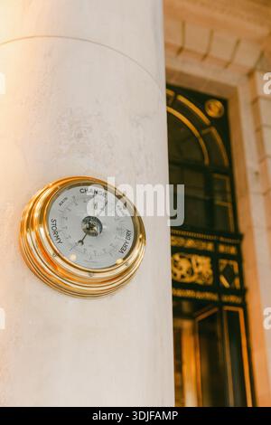 Un barometro montato su una colonna mostra gli indicatori meteo vicino a un ingresso decorativo della città. Foto Stock