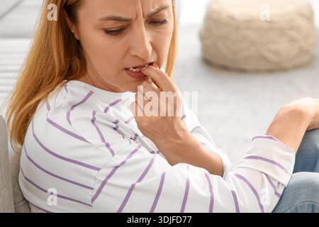 Donna matura preoccupata che morde le unghie a casa Foto Stock